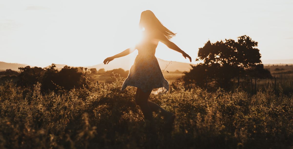 Woman dancing in a summer field during sunset
