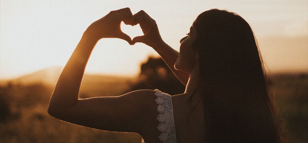Woman making heart sign with her fingers during sunset